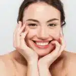 Smiling woman with clear skin touching her face.